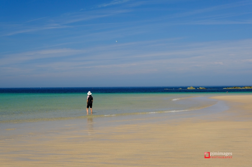 Woman in white hat paddling in the shallow water on Godrevy beach in Cornwall